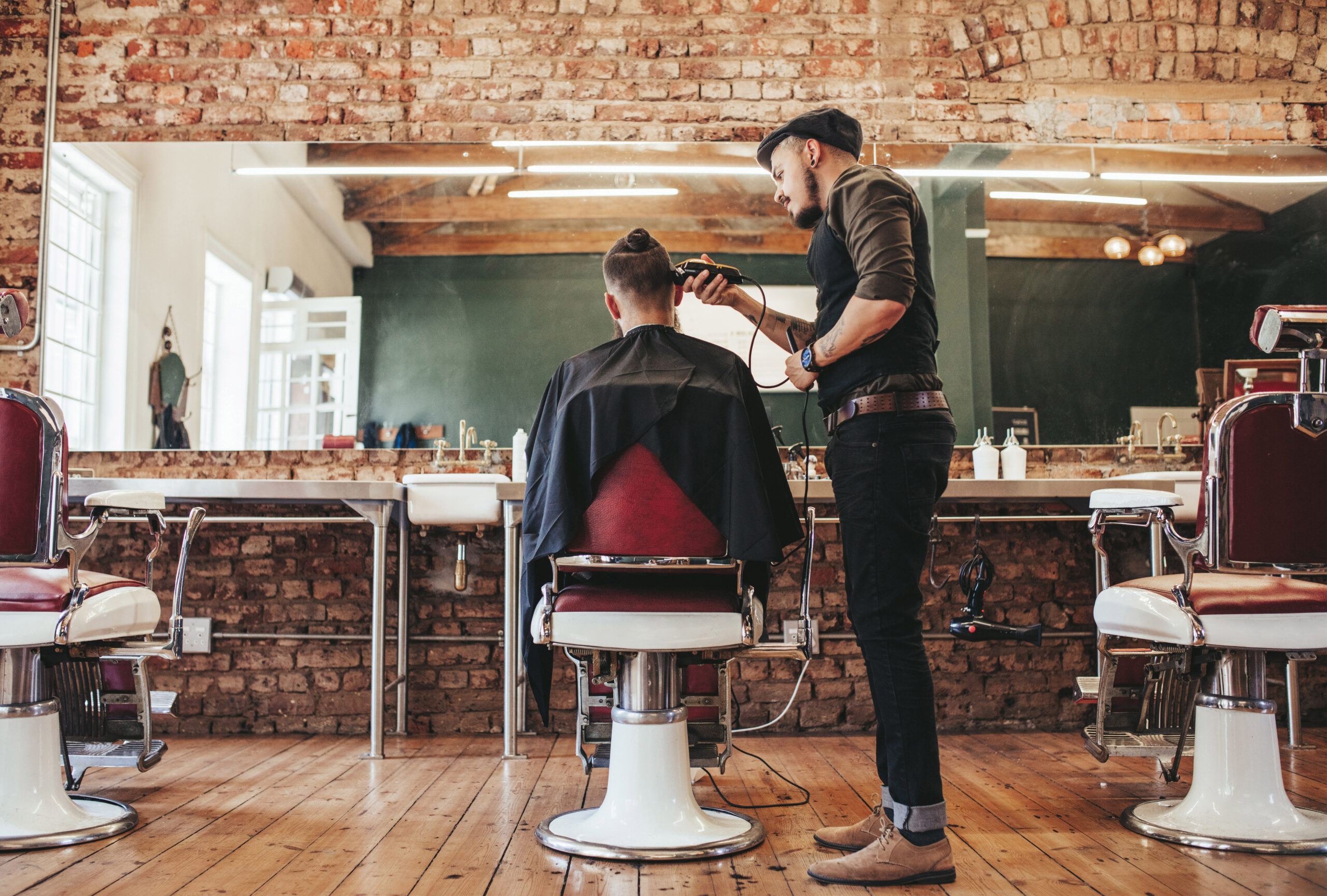 Rear view shot of handsome hairdresser cutting hair of male client. Hairstylist serving client at barber shop.