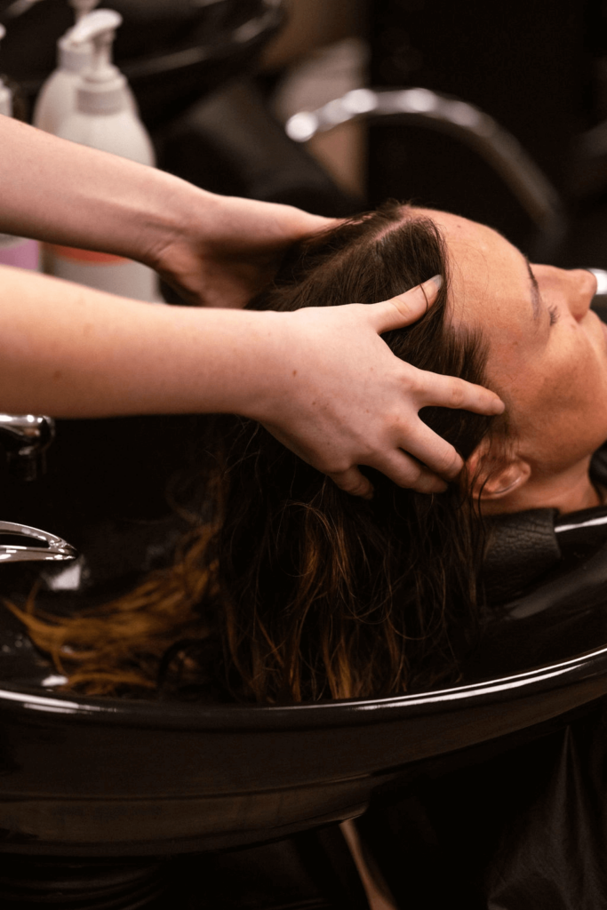 Demi Apprentice washing client's hair in hairdressing basin
